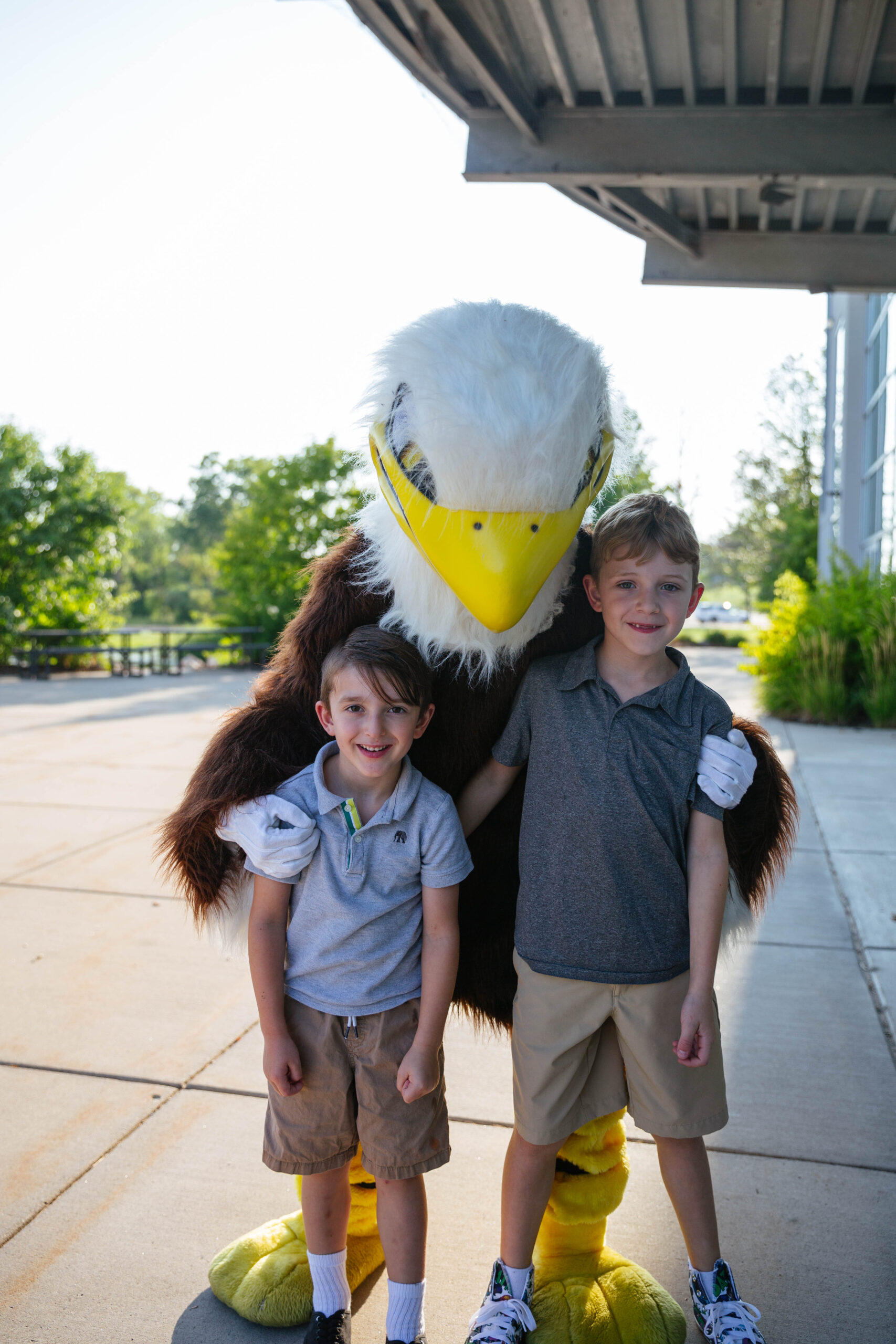 Soarin, New Life's Eagle Mascot, posing with two young boy students outside the main doors of NLA.