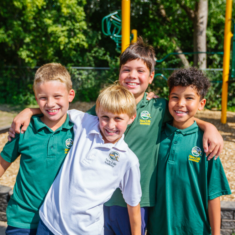 Four Lower School boys outside at the New Life playground smiling at the camera